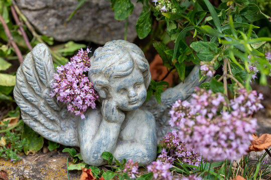 Engelsfigur aus Stein zwischen Blumen im Garten