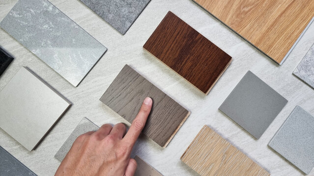 interior designer's hand choosing material samples including wooden engineering flooring tiles, grainy quartz stones, concrete tiles, wooden vinyl flooring tile, marble artificial stone. mood board.