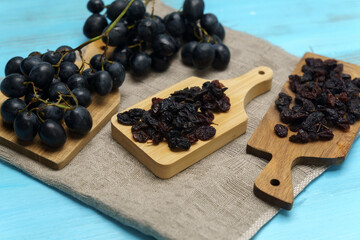 Organic dry fruits dried black grapes or black raisins on blue wooden surface.