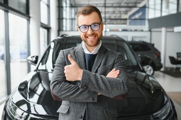 Good looking, cheerful and friendly salesman poses in a car salon or showroom.