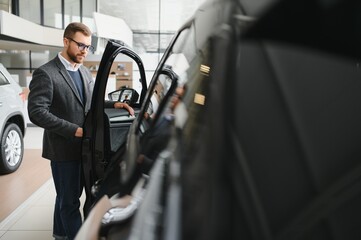 Naklejka premium Man adult customer male buyer client wears classic suit white shirt chooses auto wants to buy new automobile touch check car in showroom vehicle salon dealership store motor show indoor.