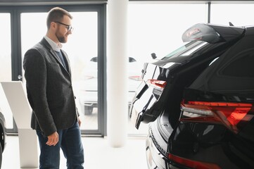 Making his choice. Horizontal portrait of a young man in a suit looking at the car and thinking if he should buy it