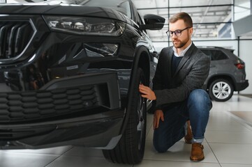 Naklejka na ściany i meble Man adult customer male buyer client wears classic suit white shirt chooses auto wants to buy new automobile touch check car in showroom vehicle salon dealership store motor show indoor. Sales concept