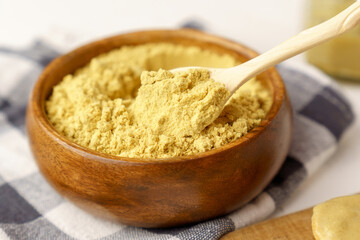 Mustard powder close up in a bowl on white table, selective focus.