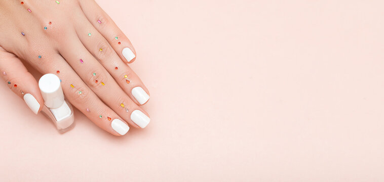 Female hand with white nail design. Glitter white nail polish manicure. Female model hand hold white nail polish bottle.