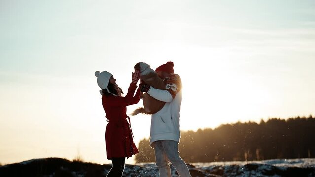 Family Christmas weekend spend time together. Happy young couple of man and woman in warm coat and hat walking in winter forest with their doggy. Love hug. Christmas eve and New Year holidays concept.