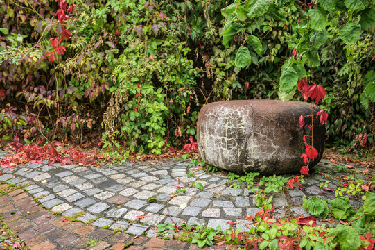 Verwitterter Mühlstein auf Pflastersteinen in Park vor herbstlichem Laub