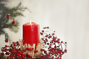 Christmas or Advent white background with a burning candle on snow, decorated with fir branches with copy space