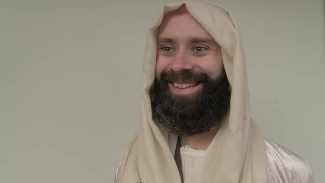 Jesus Christ, young pensive bearded man smiling, cheerful guy 30 years in light vestment, beige cape stands in image of Savior, concept Holy Scriptures of Old and New Testaments, forgiveness of sins