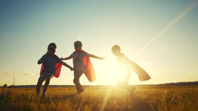 team superhero. a group of children are running across the field in a superhero costume with a silhouette of a red cape at sunset. the concept teamwork of a happy family childhood. superhero dream