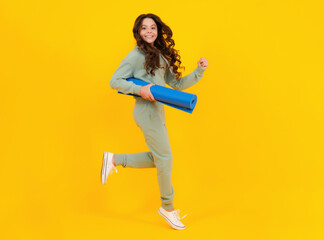 Fototapeta na wymiar Teen girl dressed in sports uniform. Teenager in a posh stylish sports suit in a hoodie with a hood hold yoga mat. Advertising sportswear tracksuit. Healthy kids lifestyle, sport. Run and jump.