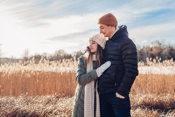 Portrait of young loving couple walking by winter river. Man and woman hugging enjoying snowy...