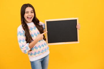 Fototapeta na wymiar School sales board. Cheerful teenage girl kid hold blackboard chalkboard with copy space on yellow background. Excited face. Amazed expression, cheerful and glad.