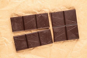 One bar of bitter dark chocolate on kraft paper, macro, top view.