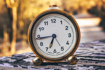 Antique clock on an old table. Blurred background where there is a road in the background
