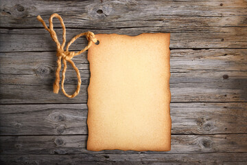 Paper label with old parchment texture, worn edges and a rope tied in the shape of a bow on a rustic wooden surface