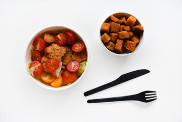Caesar salad with tomatoes and breadcrumbs in containers. Delicious breakfast with accessories on a white background. Salad with meat and breadcrumbs.
