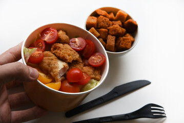 Caesar salad with tomatoes and breadcrumbs in containers. Delicious breakfast with accessories on a white background. Salad with meat and breadcrumbs.