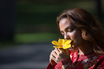 Beautiful young woman in a typical Moroccan red suit, embroidered with gold and silver threads, smelling a yellow pacific flower. Concept beauty, ethnicity, typical suits, Marrakech, Arab.