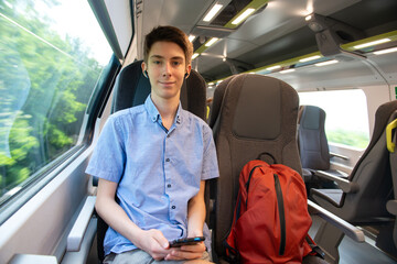 Handsome cheerful teen boy riding a train and using a smartphone