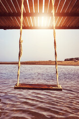 An old wooden swing at a beach, getaway concept, color toning applied.