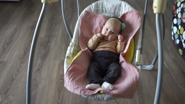 Cute baby girl swinging in electric swings at home. Happy childhood and lifestyle concept