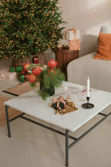 Stylish home with Christmas decorations on table and tree in the background. Festive decorations for winter holidays celebration. 