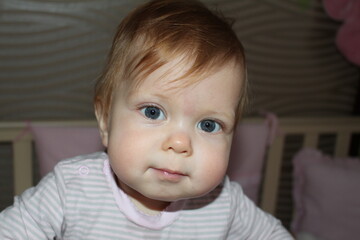 Cute little girl standing in the crib and looking at the camera