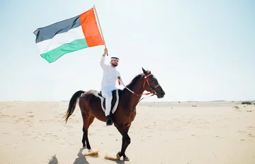 Foto op Plexiglas Young adult with Kandura, the emirates traditional clothes, riding his horse in the desert © oneinchpunch