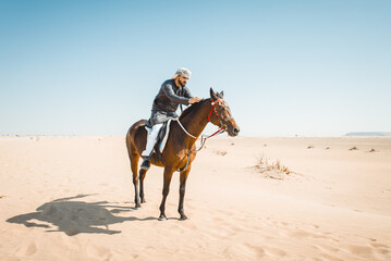 Young adult with Kandura, the emirates traditional clothes, riding his horse in the desert