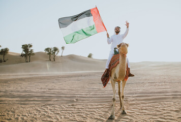 Man wearing traditional clothes, taking a camel out on the desert sand, in Dubai - obrazy, fototapety, plakaty