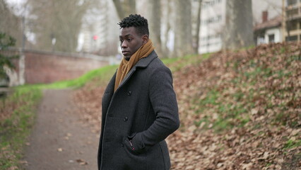 Pensive black man standing outside in cold winter season wearing scar and coat