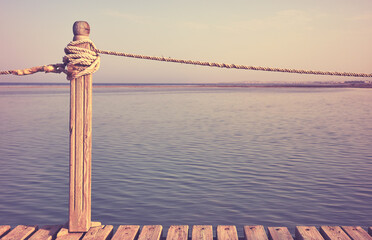 Fototapeta premium Wooden pier rope railing, selective focus, color toning applied.