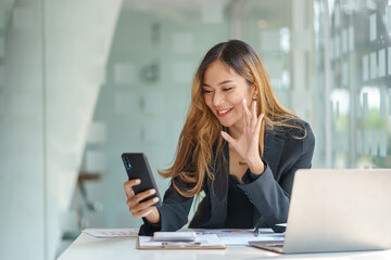 Cute young Asian business woman talking and video conferencing on mobile phone with customer at work.