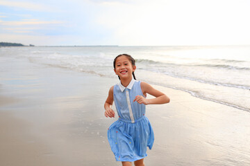 Fototapeta na wymiar Portrait of Asian young girl kid running on tropical sand beach at morning sunrise.