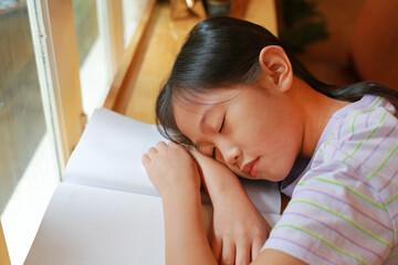 Asian young girl child sleeping on a book near the windows. Education and resting concept.