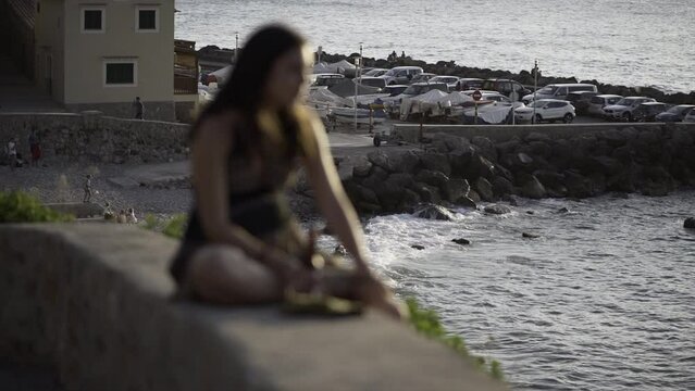 Defocused girl sitting next to the seaside looking at the horizon at sunset in Mallorca.