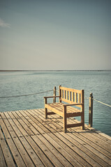 Fototapeta na wymiar Wooden bench at a pier, retro style toning applied.