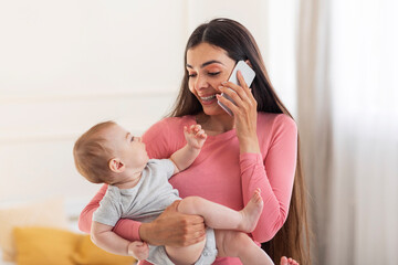 Young mother's lifestyle concept. Happy mom talking on cellphone, holding baby in arms and having phone conversation