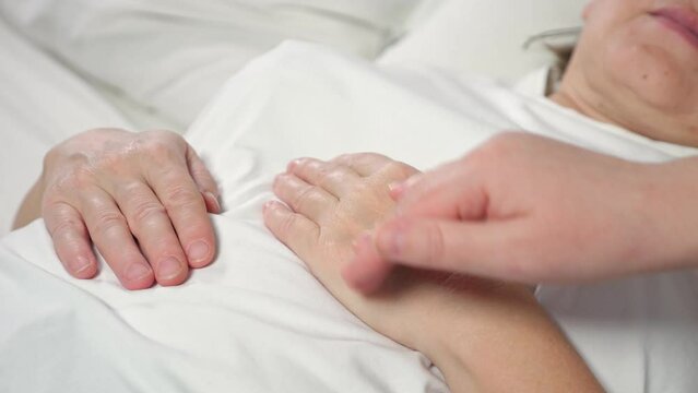 Daughter strokes hand of sick mother lying in bed at home. Woman takes care of elderly bedridden mom after difficult surgery showing support closeup