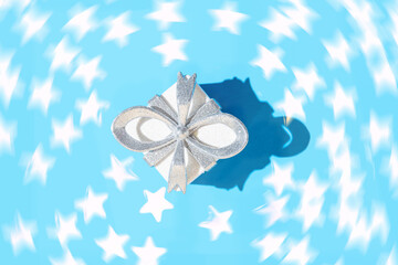 Creative composition made with glittering white present box with silver bow on pastel blue background with flying stars. Christmas or birthday gift concept. Holiday theme. Minimal style.