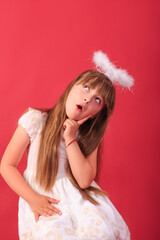 A little blue-eyed girl in a white angel dress against a red background. Studio shot of a baby girl in an angel dress.