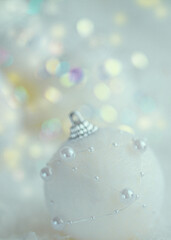 Christmas white ball with pearls on white snow. Blurred background with beautiful bokeh. Shallow depth of field. Toned image. Copy space. Airy atmosphere. Art photography. Soft focus. Close-up.