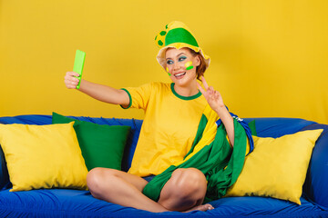 Caucasian woman, redhead, Brazilian soccer fan, on couch taking self portrait with smartphone
