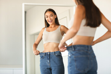 Successful slimming concept. Excited caucasian lady wearing jeans after weight loss, comparing...