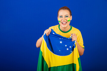 Caucasian woman, redhead, Brazil soccer fan, Brazilian, blue background, screaming goal with flag...