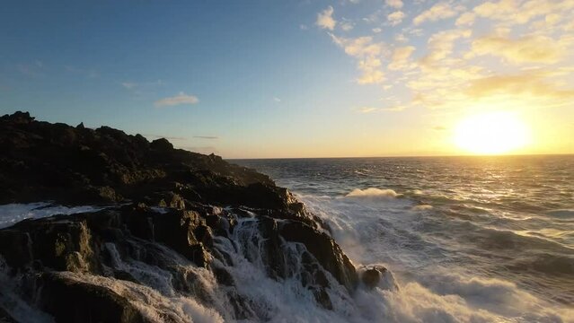 Aerial view flight very close up foamy spray waves ocean crash rocky shore by sunset rock