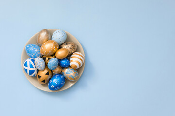 Stylish Easter golden decorated eggs on grey plate isolated on blue background. Trendy flat lay easter. Happy Easter card with copy space for text. Minimal easter concept.