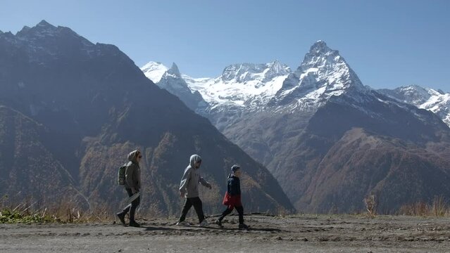 Family walks on background of mountain valley with snowy peaks. Creative. Women with child are walking in mountain valley on sunny day. Family hiking with child in valley with rocky mountains