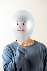 Woman dressed in blue with a balloon on her head with a sad face drawn on her head.